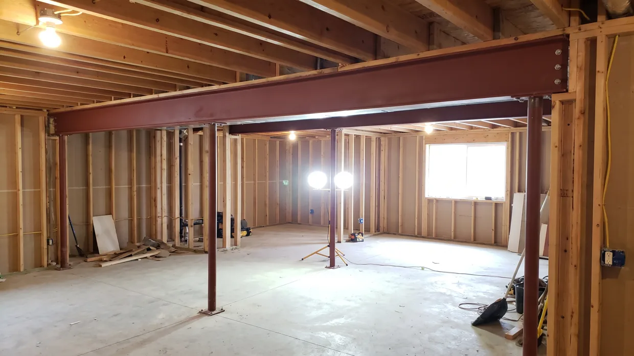 Newly installed steel beam spanning an open basement ceiling where a load-bearing wall was removed